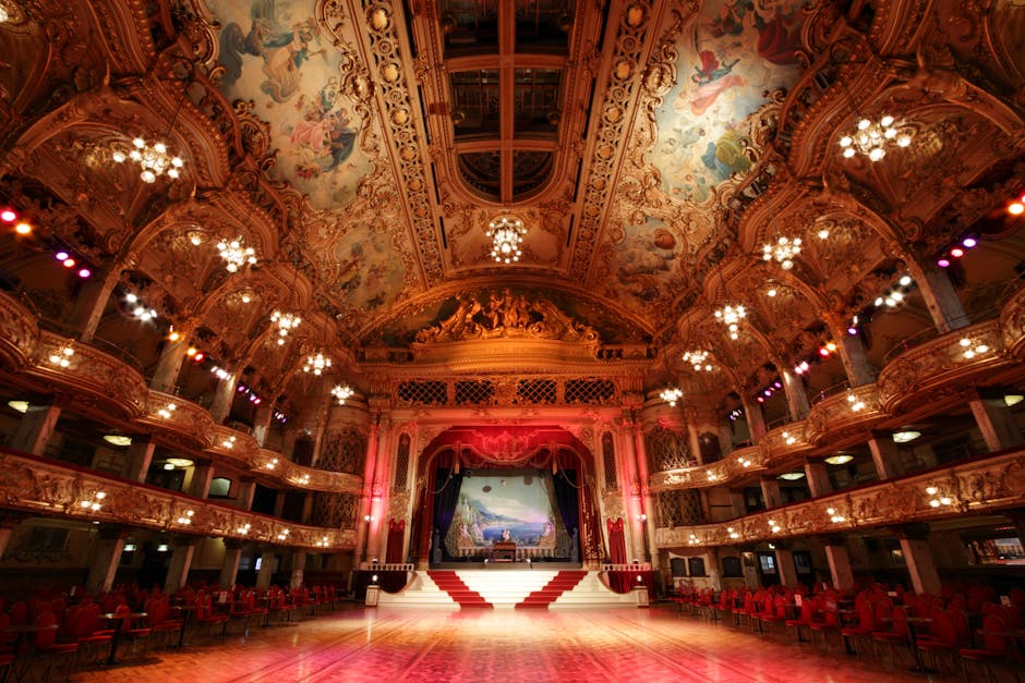 Interior of a theatre or event space featuring rows of plush, burgundy upholstered chairs arranged neatly on a level floor, with a large window at the back allowing natural light to enter. Light-colored stone or brick walls, along with heavy, dark curtains framing the window, add to the elegant atmosphere. The space appears clean and well-maintained, with no visible dust or stains on the seating or floor. Croydon Carpet Cleaning has performed surface cleaning and maintenance, ensuring a hygienic environment suitable for events at Fairfield Halls in Croydon.